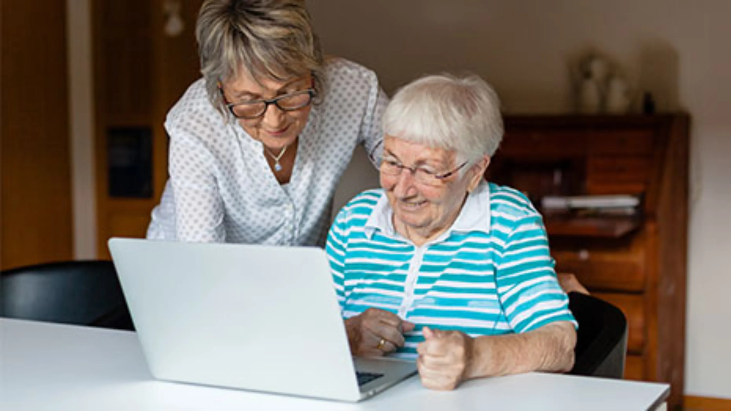 Eine Frau hilft einer Seniorin mit dem Laptop
