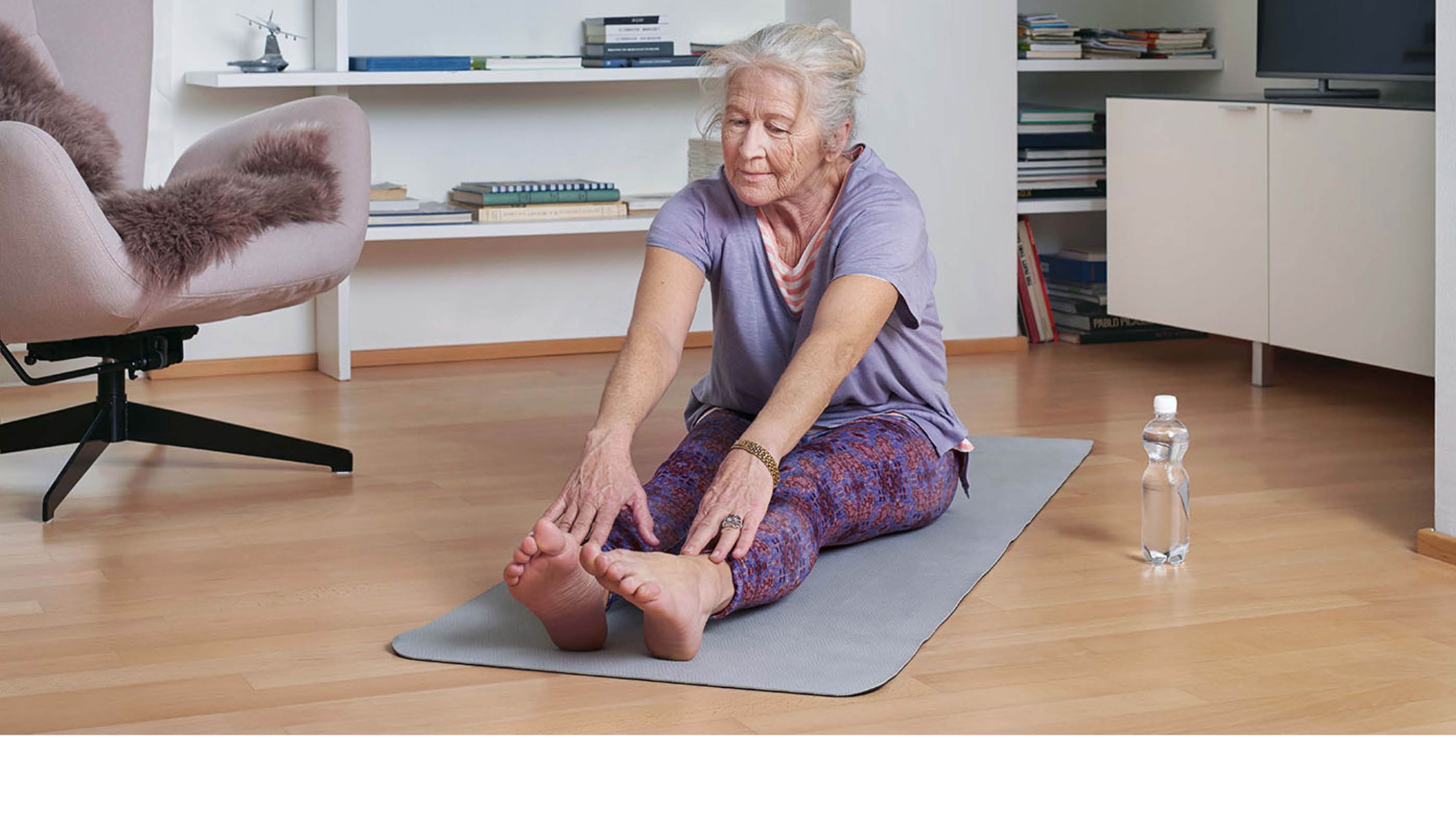 Seniorin sitzt auf Yogamatte und macht Dehnübungen.