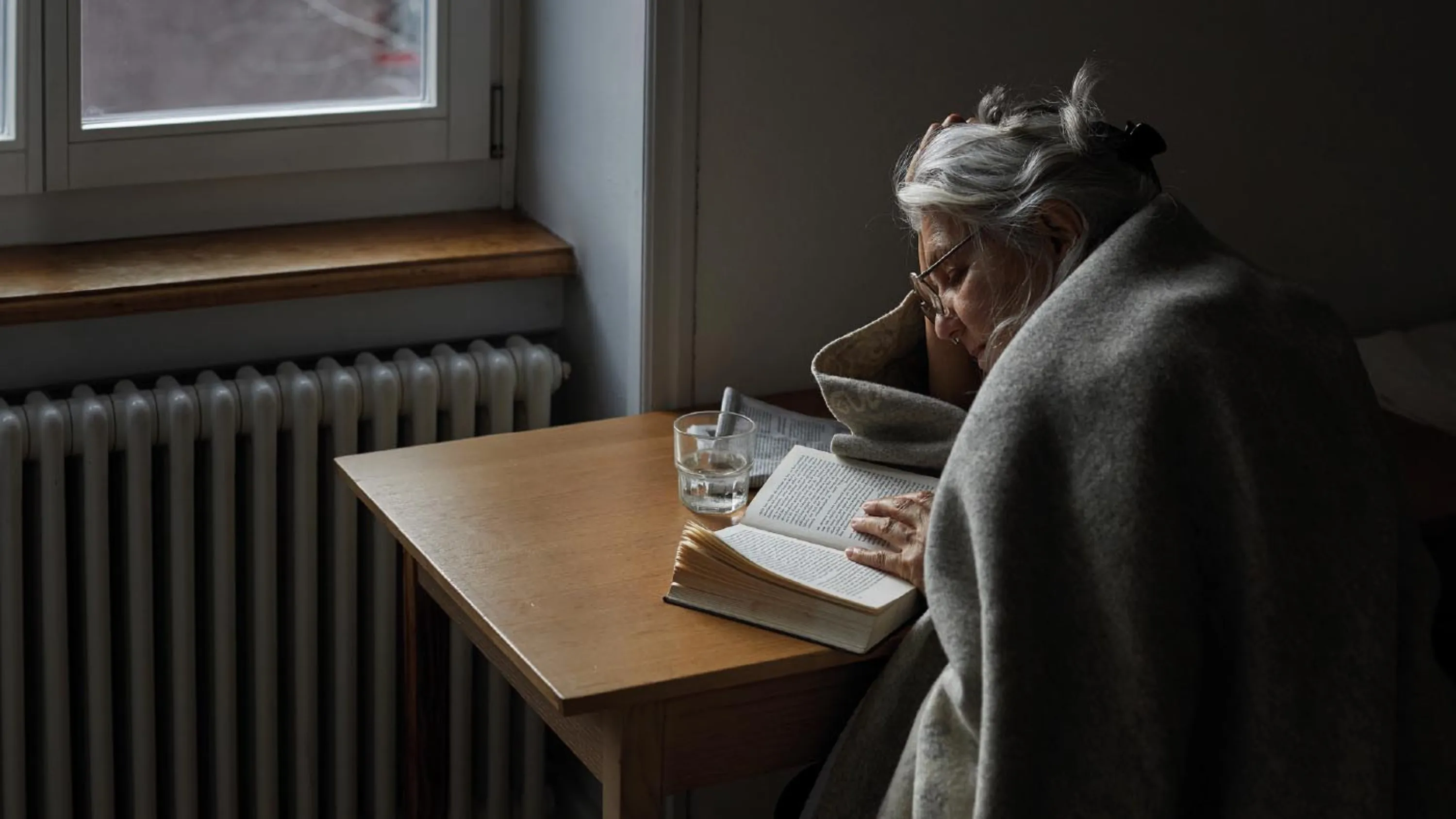 Ältere Frau sitzt am Tisch und liest in einem Buch.