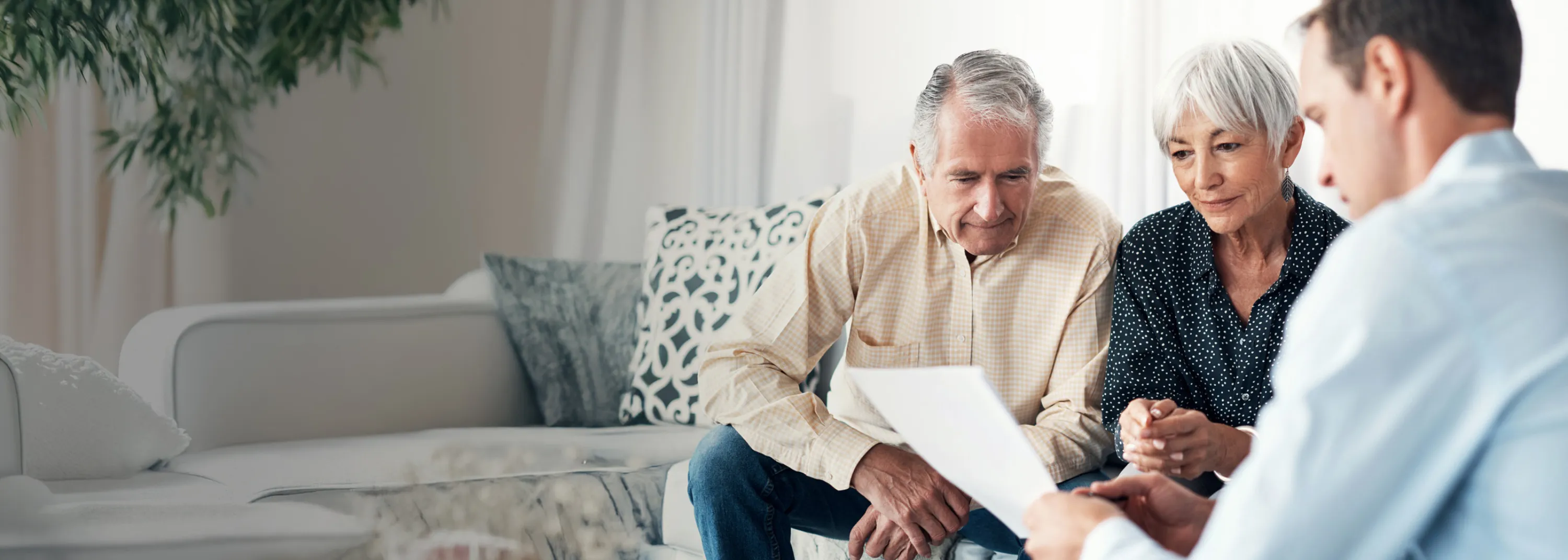 Una coppia e un notaio sono seduti su un divano e stanno esaminando un testamento.