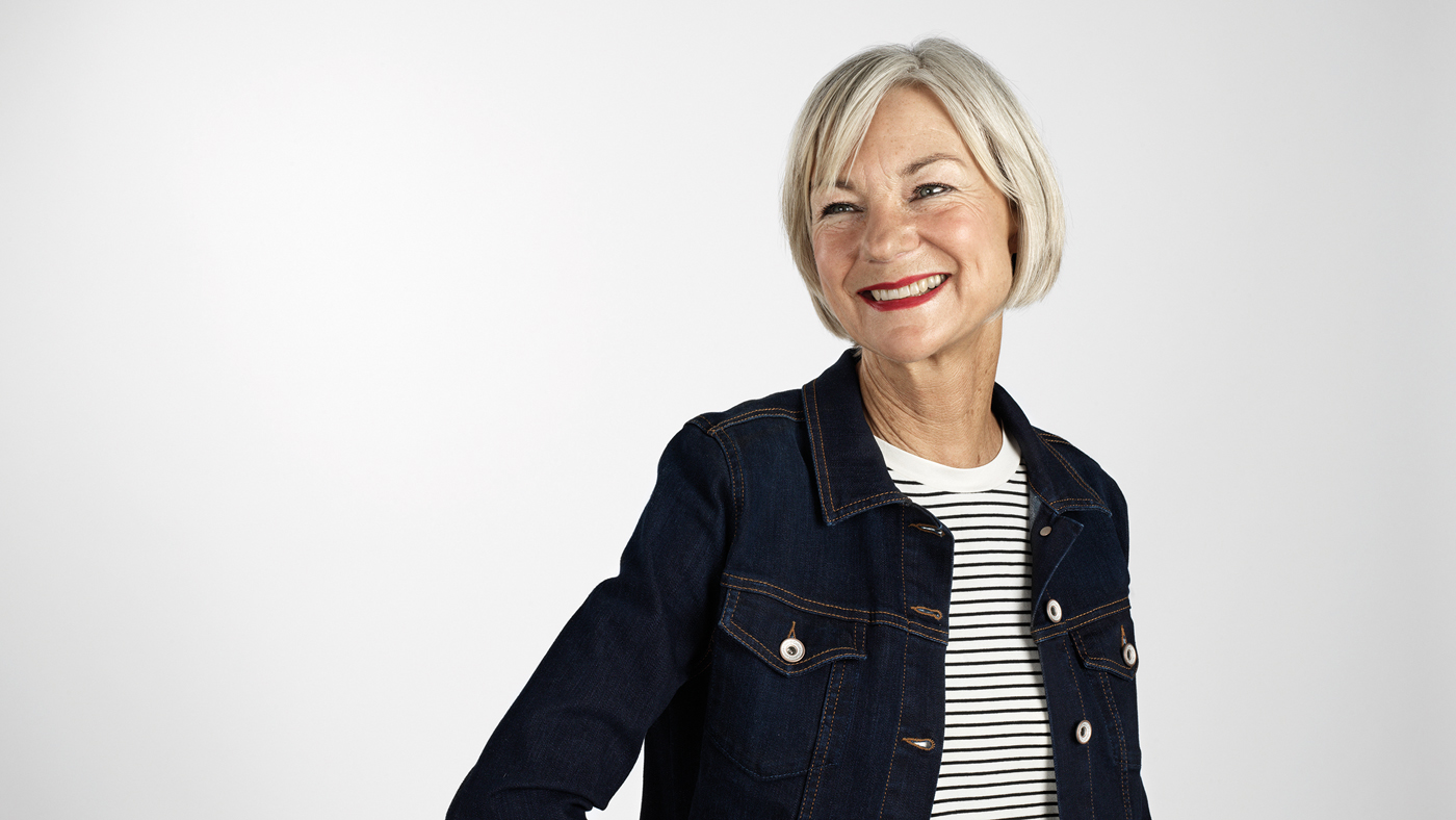 Una donna anziana, sorridente, con i capelli grigi e una giacca di jeans nera.